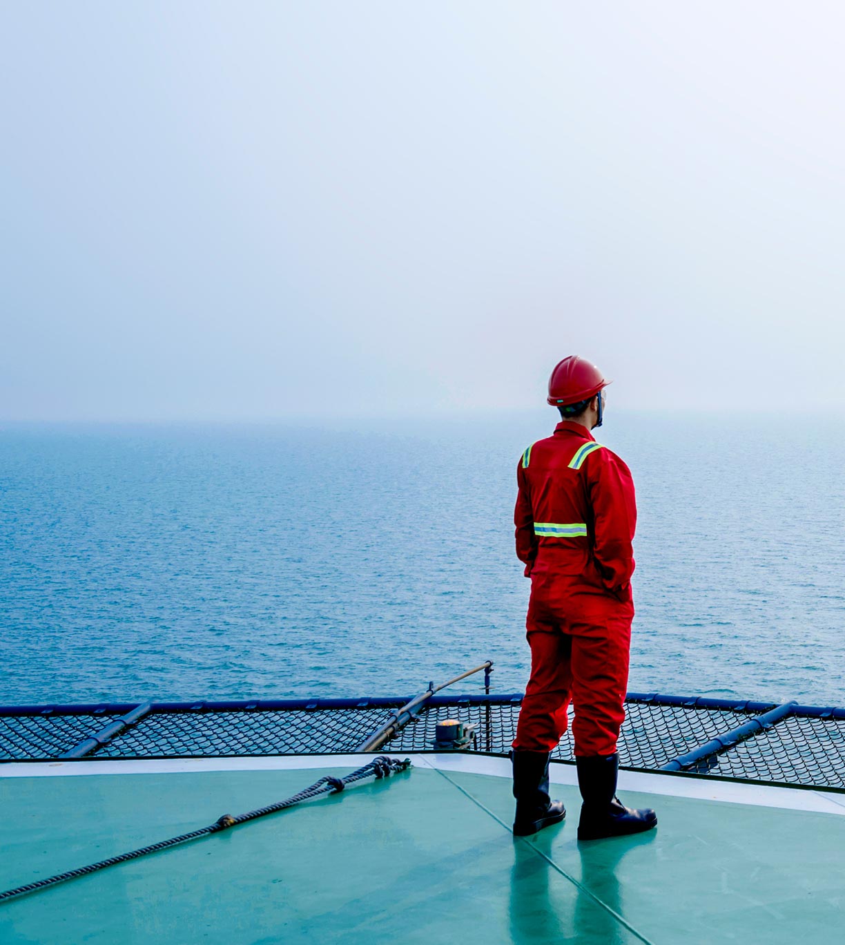 Woman from behind in orange jumpsuit and hard hat on helipad